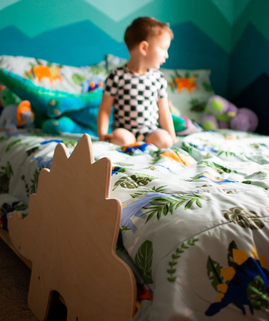 A solid wood platform bed designed for young adventurers, featuring playful dinosaur-shaped railings. The bed frame is crafted from durable, natural wood with a smooth finish, offering a safe and imaginative sleeping space for children who love dinosaurs.