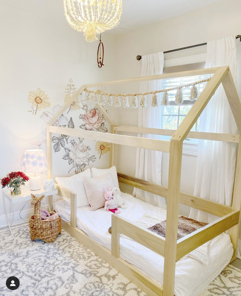 An adorable toddler bed with a low wooden frame, featuring safety rails on each side to prevent falls. The bed is adorned with colorful cartoon-themed bedding, including pillows and a soft blanket. Placed in a cozy bedroom corner with stuffed animals scattered around, creating a warm and inviting atmosphere for a young child's sleep space.