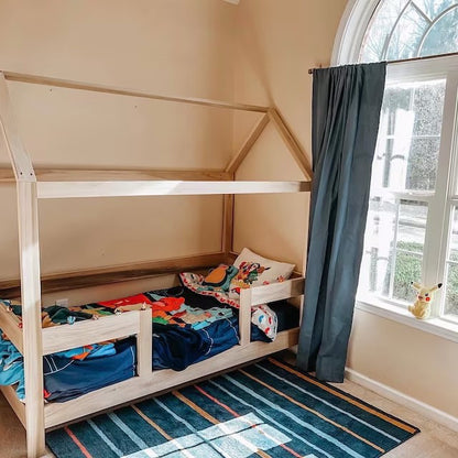 An adorable toddler bed with a low wooden frame, featuring safety rails on each side to prevent falls. The bed is adorned with colorful cartoon-themed bedding, including pillows and a soft blanket. Placed in a cozy bedroom corner with stuffed animals scattered around, creating a warm and inviting atmosphere for a young child's sleep space.