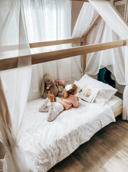 A charming house-shaped children's bed crafted entirely from natural wood, featuring a cozy and inviting design. The bed resembles a miniature house, complete with a peaked roof, window cutouts, and a sturdy wooden frame. Inside, a comfortable mattress is adorned with soft bedding, providing a cozy spot for children to sleep and play. With safety rails along the sides for added security, this wooden house bed creates a whimsical and imaginative sleep space for young ones to enjoy in their bedroom.