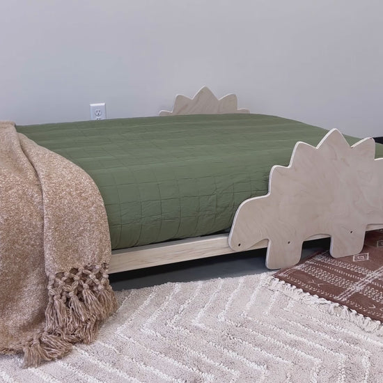 A solid wood platform bed designed for young adventurers, featuring playful dinosaur-shaped railings. The bed frame is crafted from durable, natural wood with a smooth finish, offering a safe and imaginative sleeping space for children who love dinosaurs.