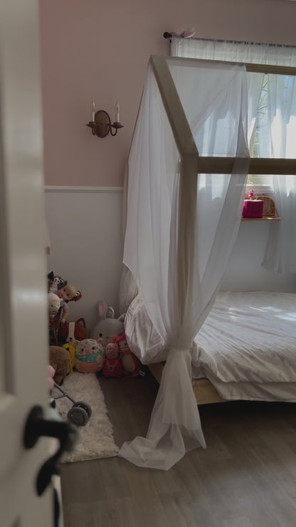 A charming house-shaped children's bed crafted entirely from natural wood, featuring a cozy and inviting design. The bed resembles a miniature house, complete with a peaked roof, window cutouts, and a sturdy wooden frame. Inside, a comfortable mattress is adorned with soft bedding, providing a cozy spot for children to sleep and play. With safety rails along the sides for added security, this wooden house bed creates a whimsical and imaginative sleep space for young ones to enjoy in their bedroom.